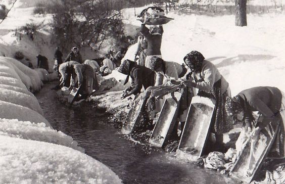 Old black and white photo of servant women washing the laundry on a creek during winter.
